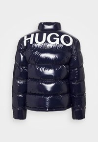 Marineblå pufferjakke med en blank finish, der har horisontale quiltede sektioner og et stort hvidt "HUGO" logo på ryggen.