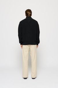 Sort strikpullover med høj krave, der har ribbede teksturer og en afslappet pasform. Parret med beige vide bukser.