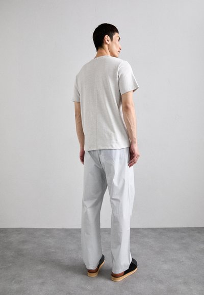 T-shirt gris clair à manches courtes associé à un pantalon gris à rayures, ample, et des chaussures noires à enfiler avec une semelle en bois.