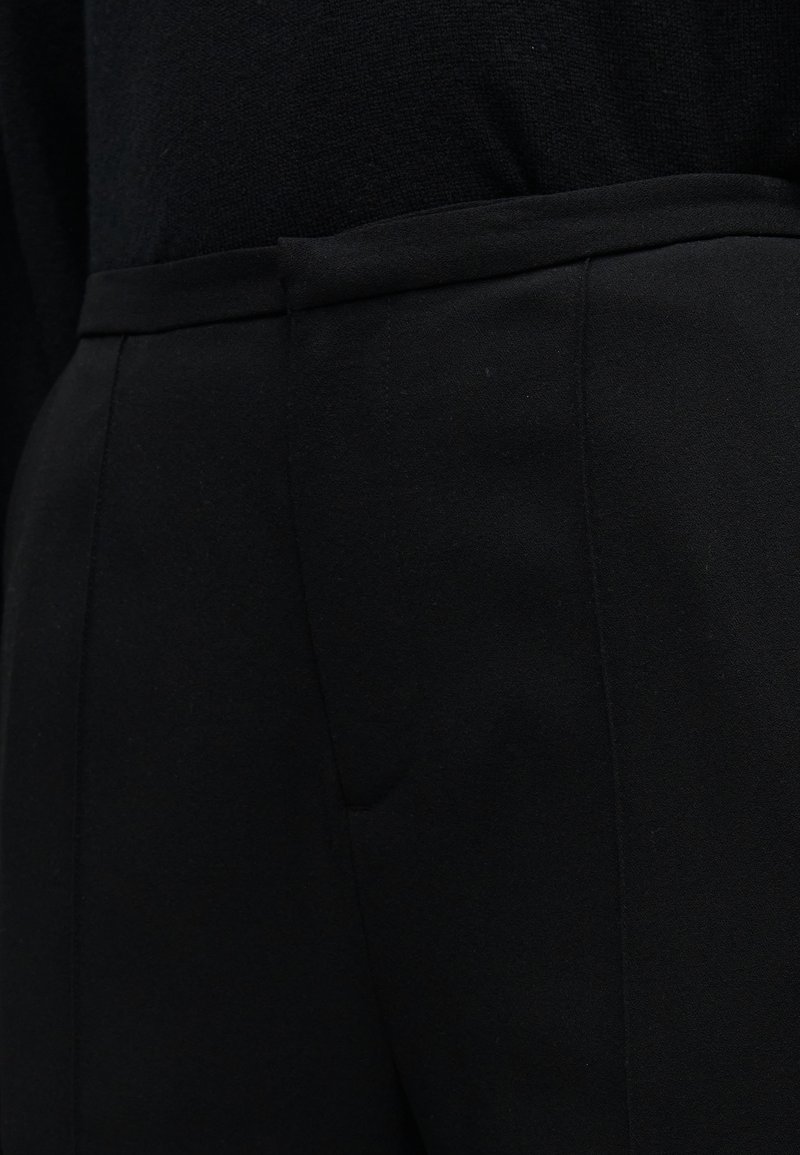 Pantalons noirs sur mesure avec une texture lisse, une coupe droite et des poches latérales discrètes, dotés d'une ceinture structurée.