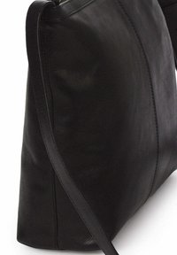 Bolso de mano de cuero negro con textura suave, forma triangular y una larga correa para el hombro. Presenta costuras minimalistas a lo largo de los lados.