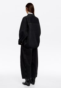 Zwarte denim oversized shirt met zilveren studs langs de naden, gecombineerd met wijde zwarte broeken en zwarte enkellaarzen.