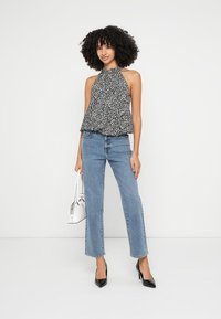 Juoda ir balta raštuota halterio stiliaus palaidinė laisvo kirpimo, derinama su aukšto liemens mėlynomis džinsinėmis kelnėmis ir juodais smailiais aukštakulniais. Papildyta balta rankine.