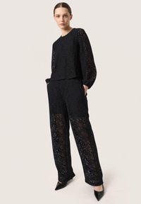Set due in pizzo nero composto da top a maniche lunghe e pantaloni dritti. Elegante motivo floreale con dettagli trasparenti, abbinato a tacchi a punta neri.