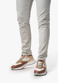 Sneaker mit einer Farbgestaltung in Beige, Weiß und Braun, hergestellt aus Mischmaterialien; strukturierte Mesh-Einsätze und Gummisohlen.