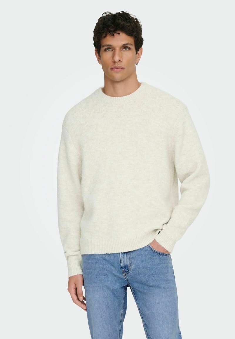 Pull tricoté beige clair avec un col rond, des poignets et un ourlet côtelés. Assorti à un jean bleu clair. Texture douce, design décontracté.