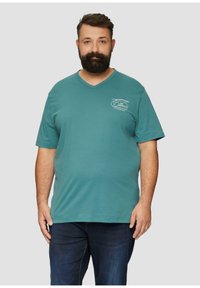 Teal katoenen t-shirt met een v-hals ontwerp. Heeft korte mouwen en een logo-detail aan de voorkant. Gepaard met donkerblauwe denim jeans.