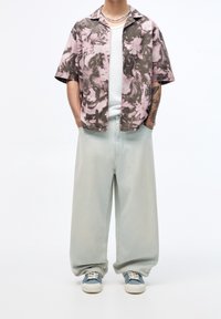 Camicia a maniche corte, a righe rosa e grigia, abbinata a jeans palazzo verde chiaro e sneakers con dettagli blu. Sotto indossa una semplice t-shirt bianca.