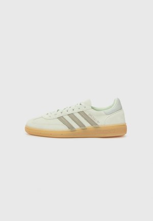 Baskets blanches Adidas Spezial avec des bandes beiges et une semelle en gomme, vue de profil, sur fond gris clair uni.