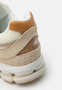 Béžové tenisky s texturovanou nubukovou kůží a koženými akcenty. Obsahují korkový detail na patě a bílou podrážku s vzduchovým odpružením.