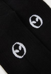 Calcetines negros con diseño de logotipo blanco. El material parece suave con una textura lisa. El logotipo presenta una forma circular con elementos curvados.