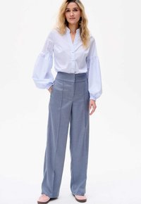 Lichtblauwe gestreepte blouse met knoopjes en pofmouwen, gecombineerd met hooggesneden, wijde grijze broeken en roze instappers.