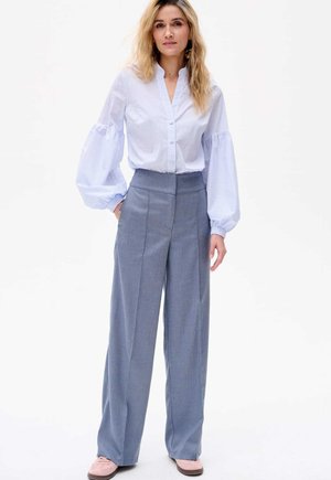 Blouse boutonnée rayée bleu clair avec des manches bouffantes, associée à un pantalon large gris taille haute et des chaussures à enfiler roses.