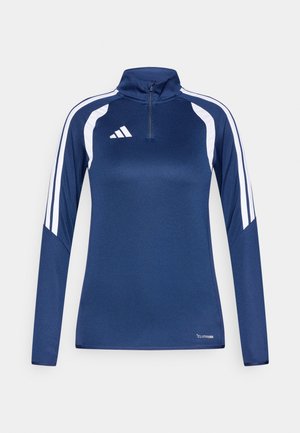 Chemise bleu marine à manches longues avec une demi-fermeture éclair, présentant des accents rayés blancs sur les épaules et un logo Adidas sur le côté gauche de la poitrine.