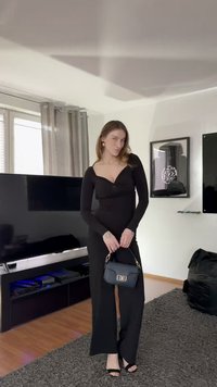 Vestido negro de manga larga con escote en v, torso ajustado y diseño de pierna ancha, combinado con un pequeño bolso azul marino con herrajes dorados.