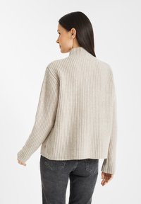Licht beige geribde trui met een hoge hals en lange mouwen, met een ontspannen pasvorm en een subtiel patroon. Gepaard met donkerblauwe jeans.