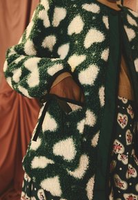 Cappotto testurizzato a motivi a cuore verde e bianco con un pelo spesso, dotato di un nastro nero legato e una gonna a motivi contrastanti sotto.