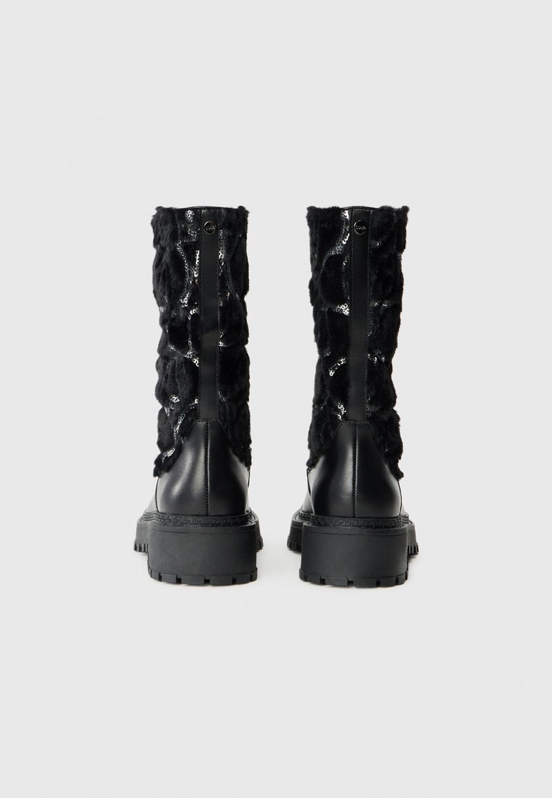 Schwarze Knöchelstiefel mit einer strukturierten, fellartigen Oberseite in glänzender Ausführung, kontrastierendem schwarzen Lederabsatz und dicker Gummisohle.