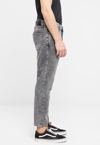 Hallid denim pükste tapered fit, kerge pesu ja viie taskuga stiil. Kombineeritud mustade tossudega, millel on valged aktsendid.