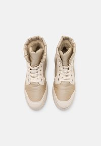 Sneaker alte beige con una toma superiore in tessuto testurizzato, collo imbottito e lacci bianchi. Presenta una suola in gomma liscia e punta arrotondata.