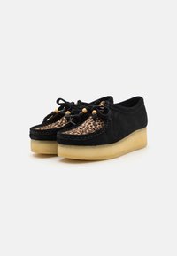 Pantofi negri din suede cu un panou din material cu imprimeu leopard, detaliu cu șireturi și mărgele din lemn, și o talpă platformă groasă din cauciuc.