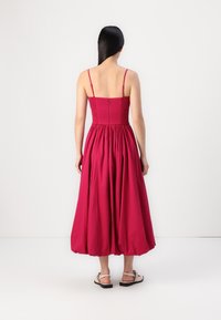 Vestido fucsia con tirantes finos ajustables, cuerpo fruncido y falda completa. La tela tiene una textura suave, con detalles fruncidos en la cintura.