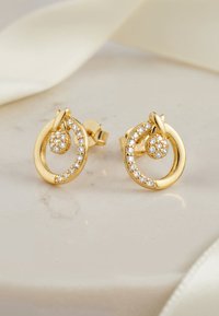 Orecchini circolari in oro con design a nodo, adornati con piccoli zirconi cubici trasparenti in una montatura a canale, su uno sfondo chiaro.