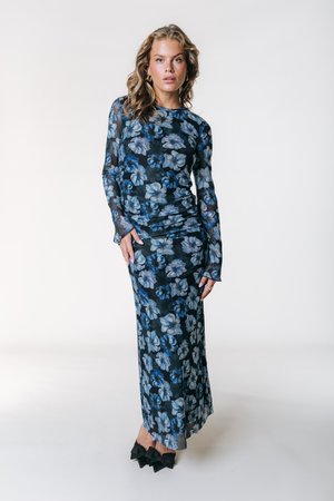 Φόρεμα με μακριά μανίκια, από διάφανο ύφασμα με λουλουδένιο σχέδιο σε σκούρο μπλε, με μοτίβα σε ανοιχτό μπλε και λευκό. Διαθέτει ραφές που δημιουργούν ρυτίδες και εφαρμοστή σιλουέτα. Μαύρα παπούτσια με φιόγκο.