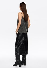 Top gris sin mangas con una textura suave, combinado con una falda larga de cuero negro. El look se completa con botas de tacón negras.