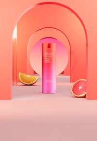 KIKO Power Shake Pearly Magic Serum i en gradient rosa flaske, plassert mellom appelsin- og grapefruktskiver mot en korallbakgrunn.