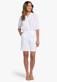 Witte, korte mouwen blouse met knopen, plooien en smockmanchetten, gecombineerd met witte op maat gemaakte shorts, beide met een gladde, lichte textuur.