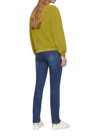 Olivgrüner Sweatshirt mit Puffärmeln und gerippten Bündchen, kombiniert mit dunkelblauen Skinny Jeans und weißen Sneakers mit metallischen Akzenten.