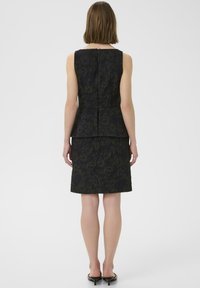 Top peplum noir à motif floral associé à une jupe ajustée, avec une texture lisse et une fermeture éclair dissimulée au dos.