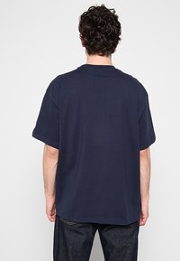 Camiseta de manga corta azul marino con un corte holgado, hecha de algodón, que presenta un cuello redondo y un detalle de costura mínima en el dobladillo.