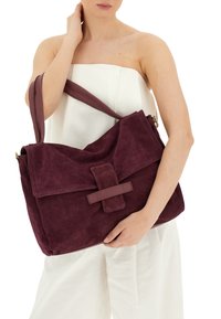 Borsa a spalla in suede bordeaux con chiusura a pattina, design sovradimensionato e tracolla piatta. Superficie testurizzata con un accento centrale a striscia.