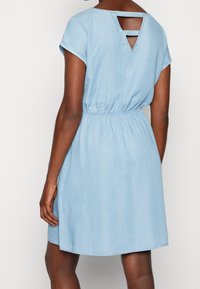 Světle modré džíny šaty s krátkými rukávy, elastickým pasem a trojúhelníkovým vykrojením na zádech. Hladká textura, délka ke kolenům.
