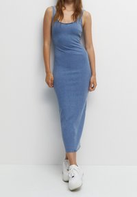 Robe midi en denim bleu clair avec une silhouette ajustée, des bretelles fines et un décolleté arrondi. Associée à des baskets blanches.