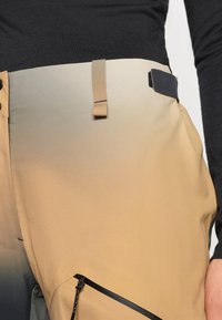 Beige és fekete, magas derekú nadrág, gradiens színátmenettel, cipzáras zsebbel és szövet övhurkokkal a deréknál. Simább anyag.