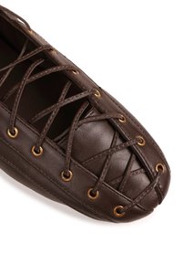 Mocassin en cuir marron avec un bout arrondi, doté de lacets croisés et d'œillets couleur or, présentant une surface texturée.