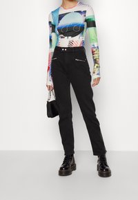 Maglietta a maniche lunghe con un design grafico multicolore, abbinata a jeans neri a vita alta con tasche con zip e stivali neri robusti.