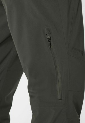 Pantalons softshell vert foncé avec une poche zippée sur le côté, texture lisse et design épuré, portant un logo sur le côté.