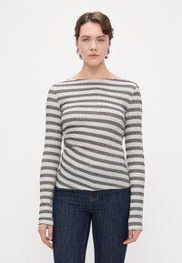 Top de rayas de manga larga en negro y crema, con escote barco y textura acanalada, combinado con jeans oscuros.