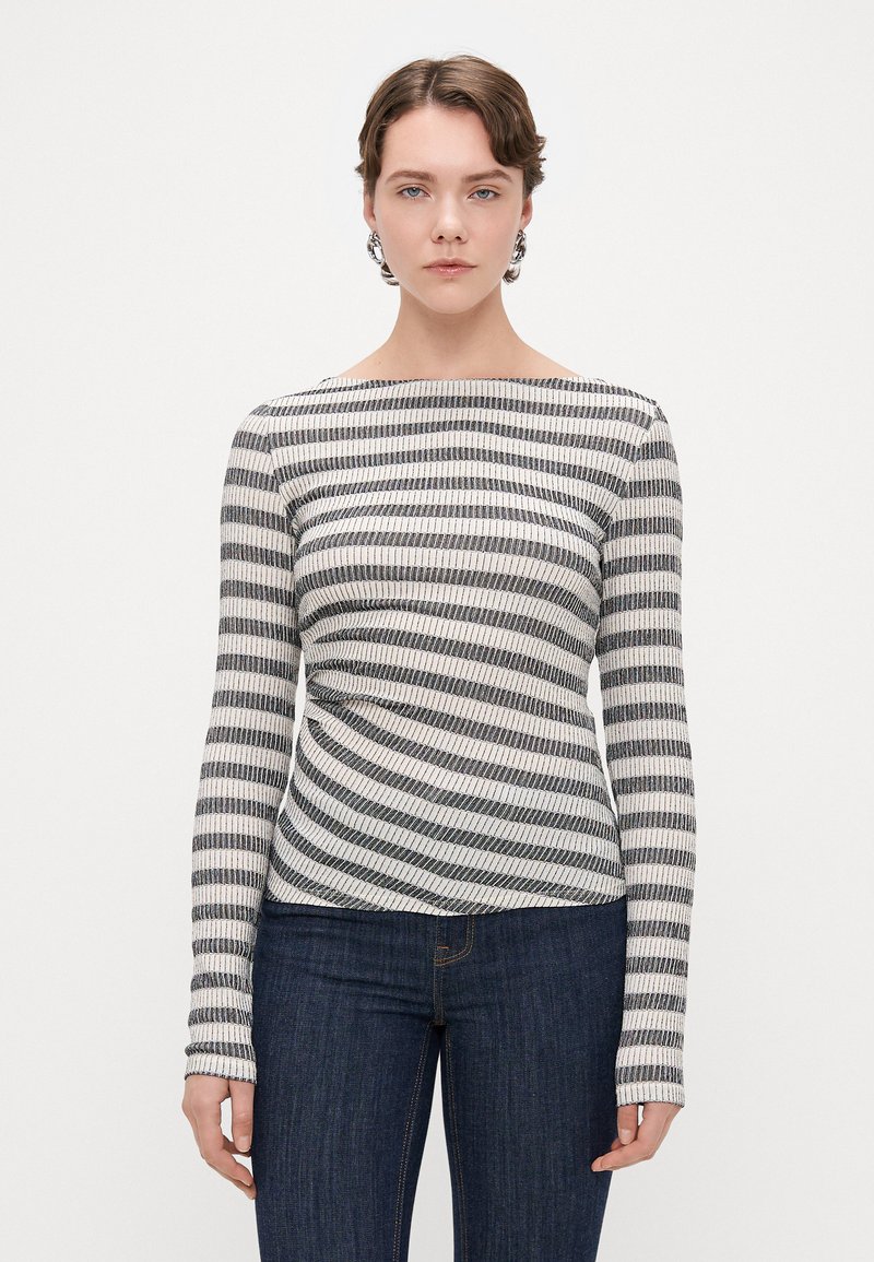 Top de rayas de manga larga en negro y crema, con escote barco y textura acanalada, combinado con jeans oscuros.