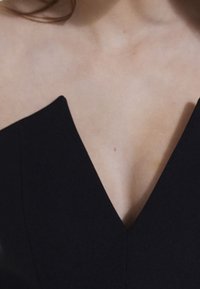 Schwarzes Kleid mit tiefem V-Ausschnitt, figurbetontem Design und glatter Textur. Der Stoff wirkt leicht und elegant und präsentiert eine klare Silhouette.