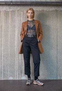 Brown snake-print long blazer, black mesh top, high-waisted black trousers, and gray sneakers with red accents. Smooth textures and tailored fit.