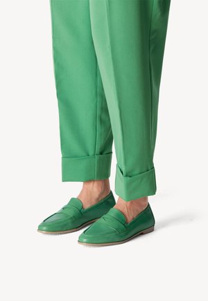 Grüne Lederloafers mit einem schlanken Design, das einen genähten Akzent auf dem Blatt aufweist. Kombiniert mit hochgekrempelten grünen Hosen.