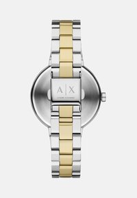 Sidabrinė ir auksinė nerūdijančio plieno laikrodis su apvaliu korpusu, grandinėlės apyranke ir išgraviruotu logotipu ant sagties. Poliruota ir šlifuota tekstūra.