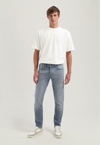 Camiseta blanca de algodón, corte relajado; jeans de mezclilla azul claro con corte ajustado; zapatillas gris y blanca; diseño simple, sin patrones visibles.