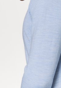 Pull tricot bleu clair avec une texture lisse et une coupe ajustée, mettant en valeur un col rond et des manches longues.