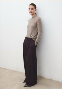 Suéter de punto beige con cuello alto, combinado con pantalones anchos de color púrpura oscuro que cuentan con pliegues frontales y bolsillos laterales.